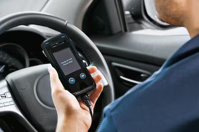 Man Blowing Into a Handheld Breathalyzer in a Car — Dore's Goodyear Autocare Tully In Tully, QLD