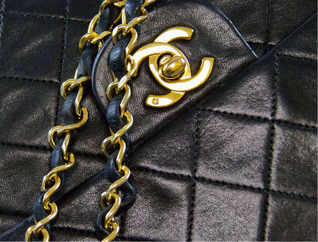 Gold Chanel logo on a black quilted leather handbag with chain strap