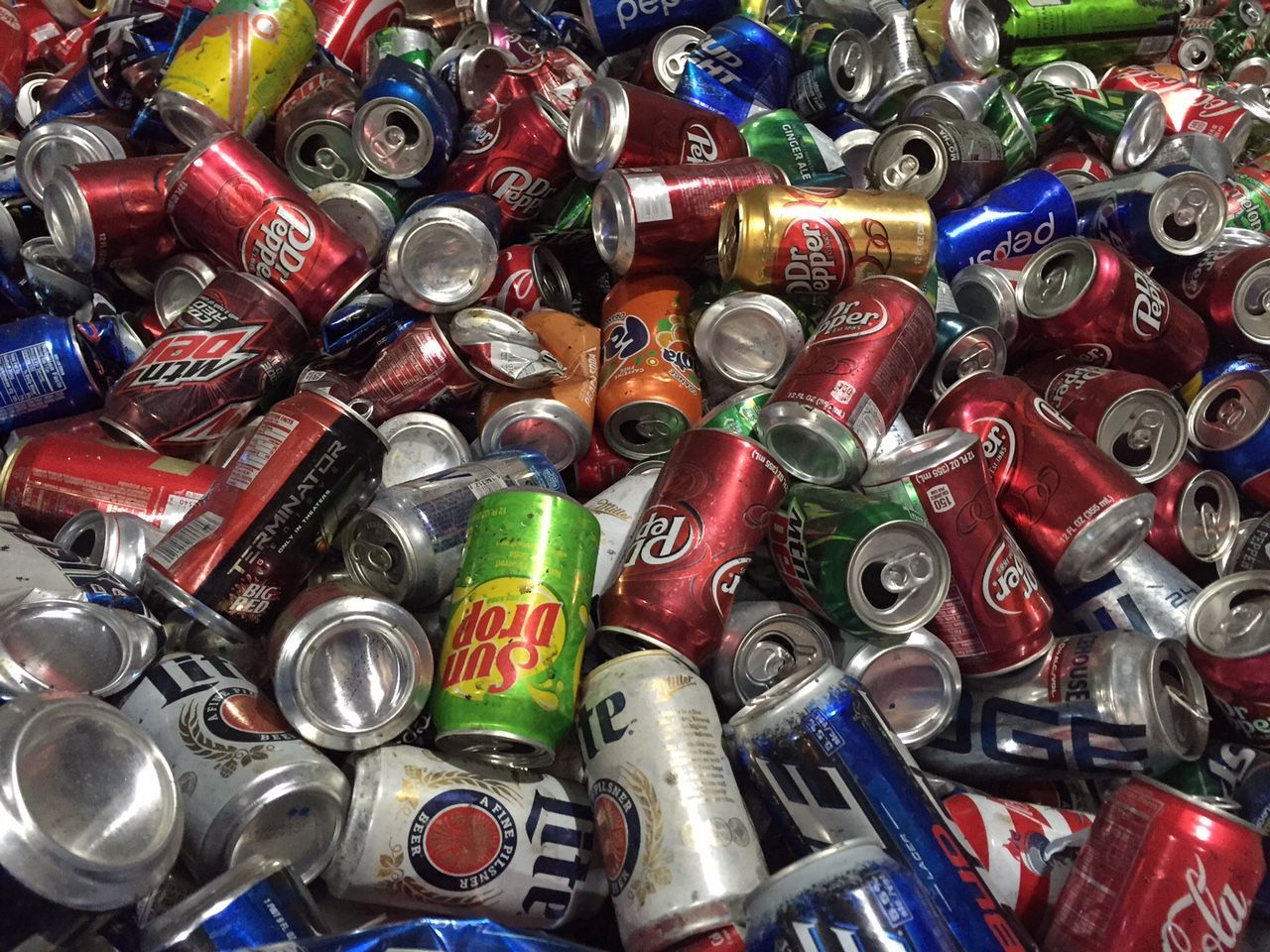 Pile of crushed aluminum beverage cans, various colors, including red, silver, and blue.