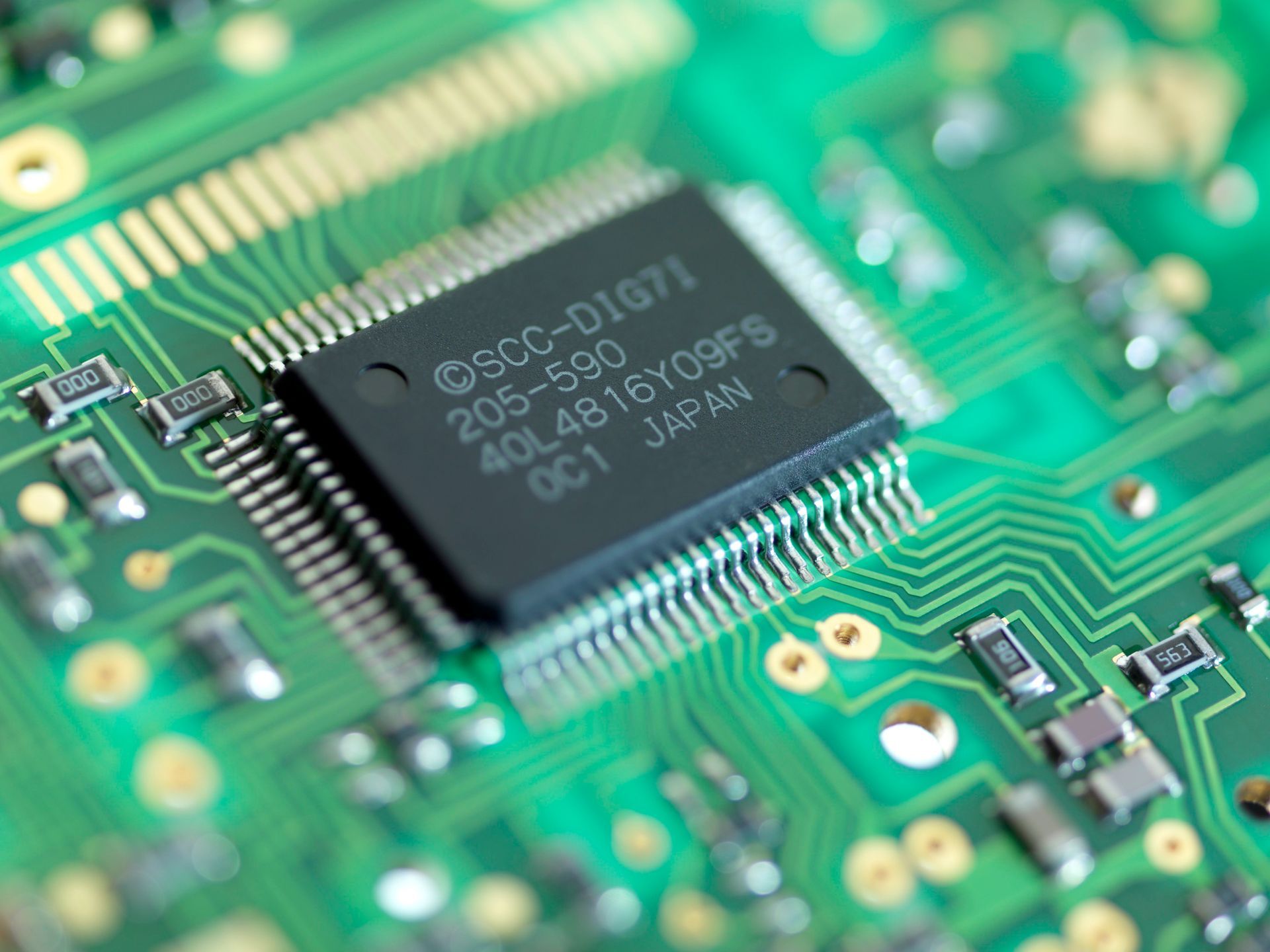 Close-up of a green circuit board with an embedded black integrated circuit chip.