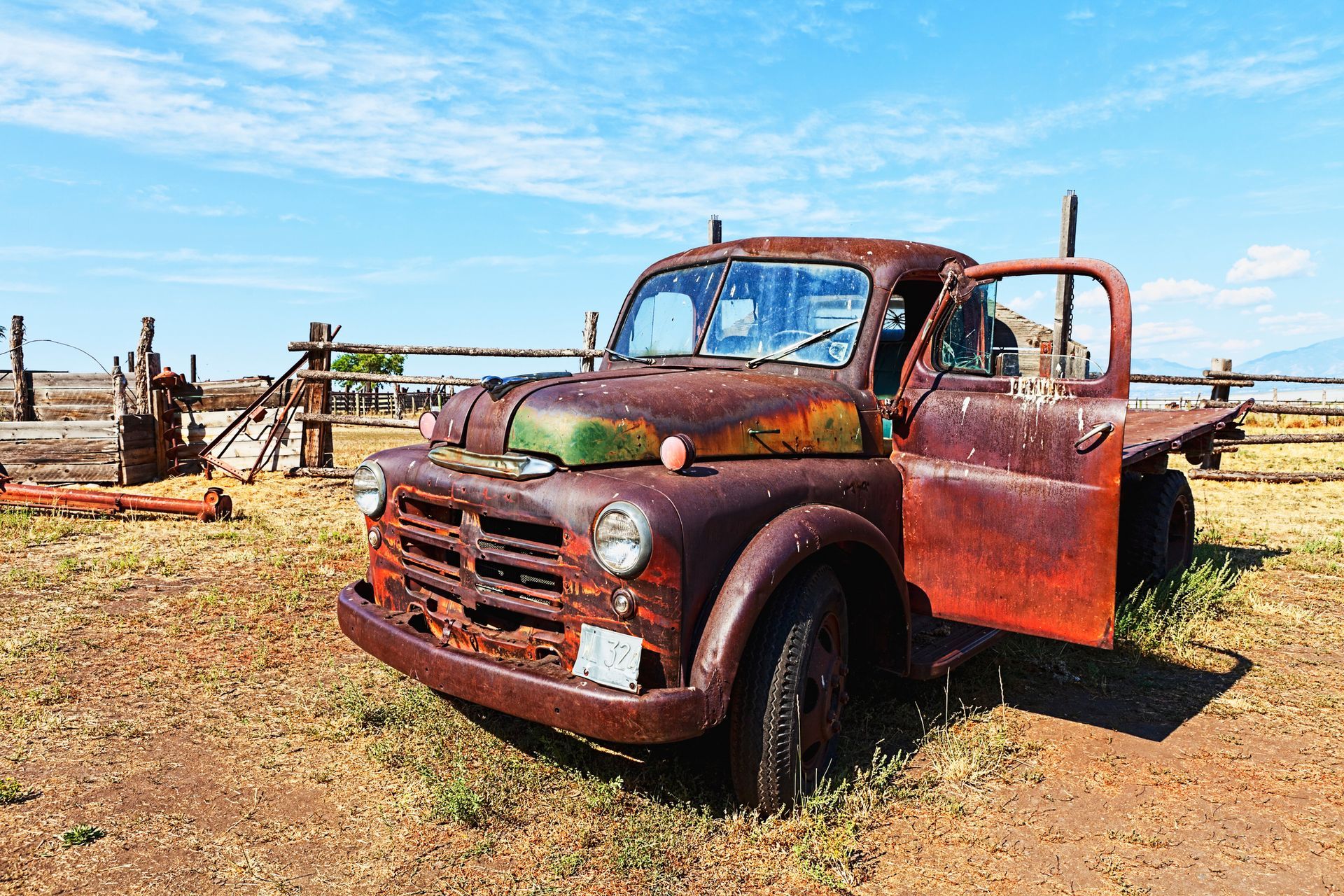 An old rusty truck is parked in a field with its doors open.