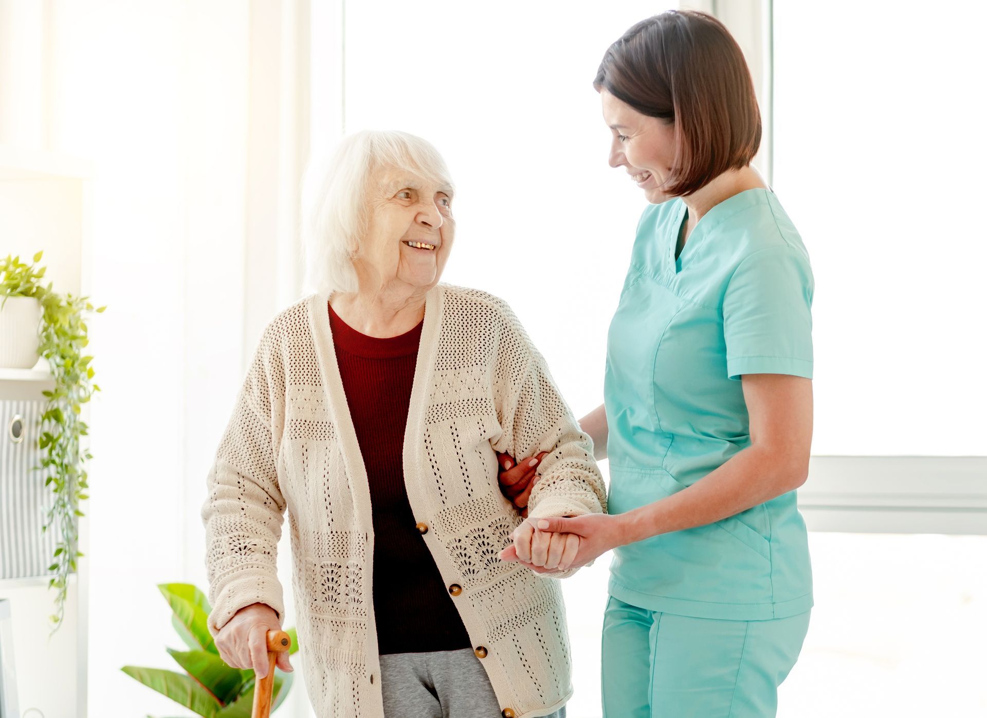 Caregiver assisting elderly person with a cane to walk; smiling indoors. Caregiver assisting elderly person with a cane to walk; smiling indoors.