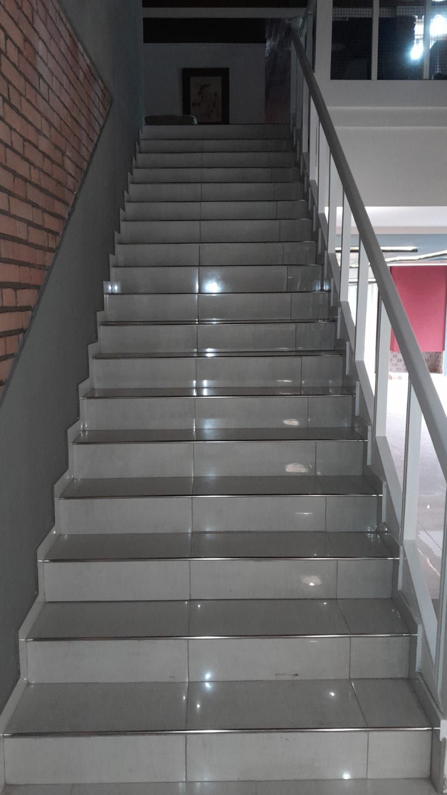 Escalera interior con peldaños de baldosas grises, una pared de ladrillo a la izquierda y una barandilla metálica