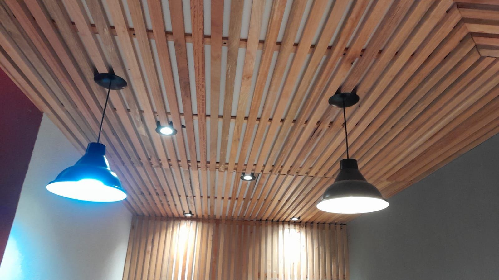 Techo con listones de madera y tres lámparas colgantes, una de ellas con luz azul, en una habitación moderna