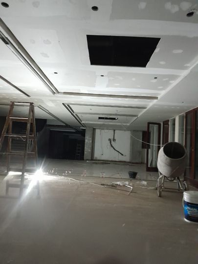 Habitación parcialmente renovada, con trabajos en el techo, una escalera, escombros y una mezcladora de cemento en el suelo