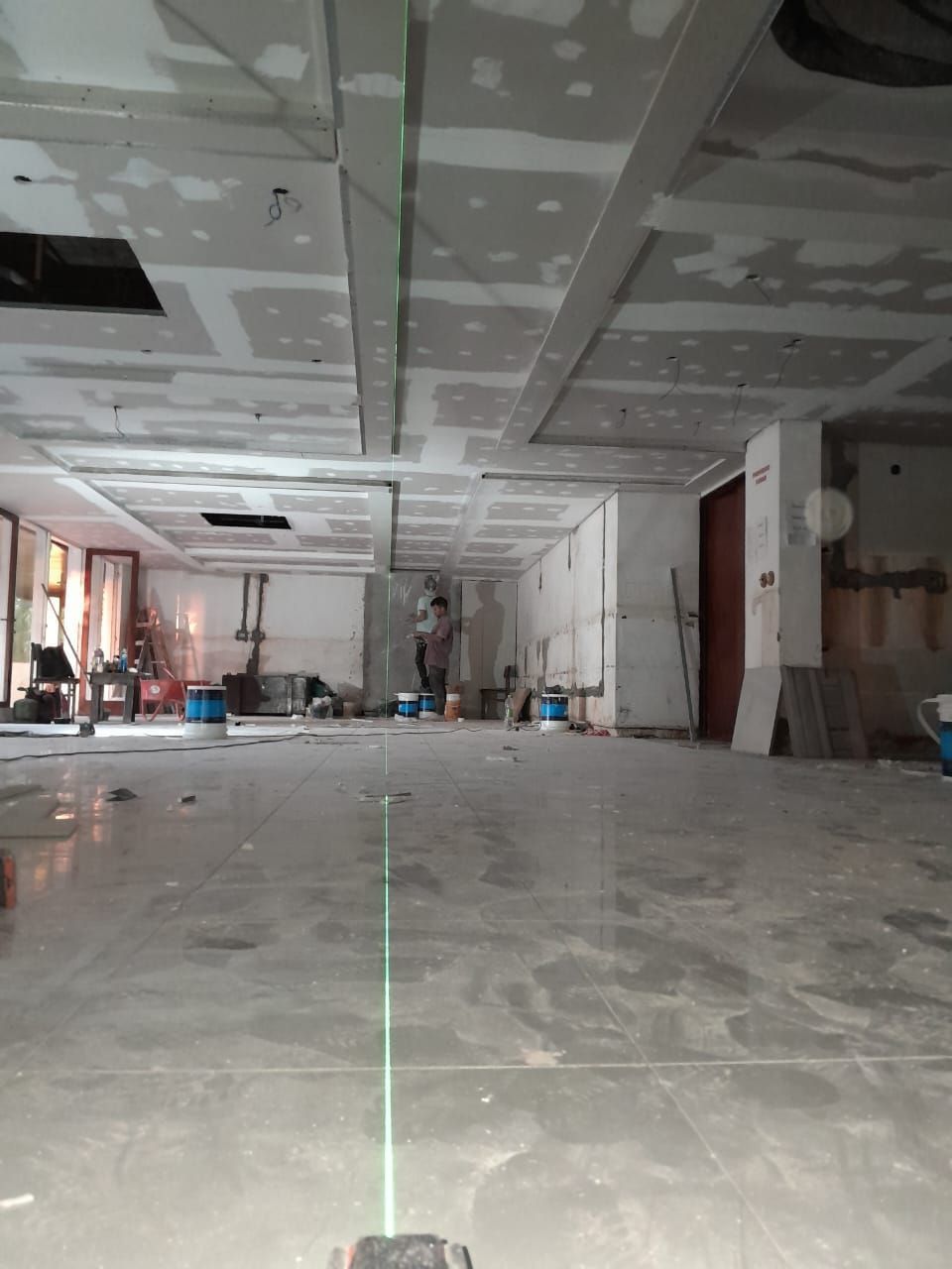 Habitación vacía sin terminar, con techo de placas de yeso, suelo de hormigón y herramientas de construcción