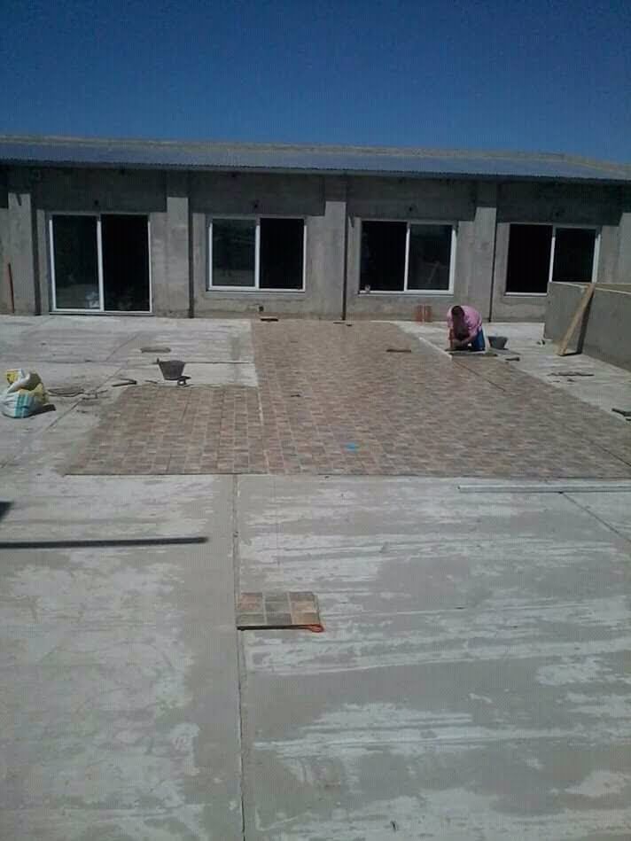 Patio de un edificio bajo con puertas abiertas y trabajadores colocando adoquines bajo un cielo despejado