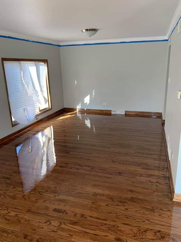 Habitación vacía con suelo de madera brillante, paredes blancas y luz del sol que entra por una ventana con persianas