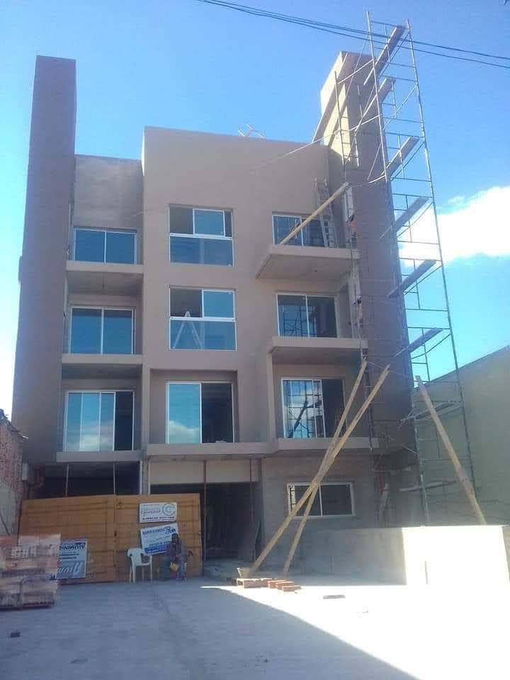Edificio de cuatro plantas en construcción, con andamios bajo un cielo azul despejado