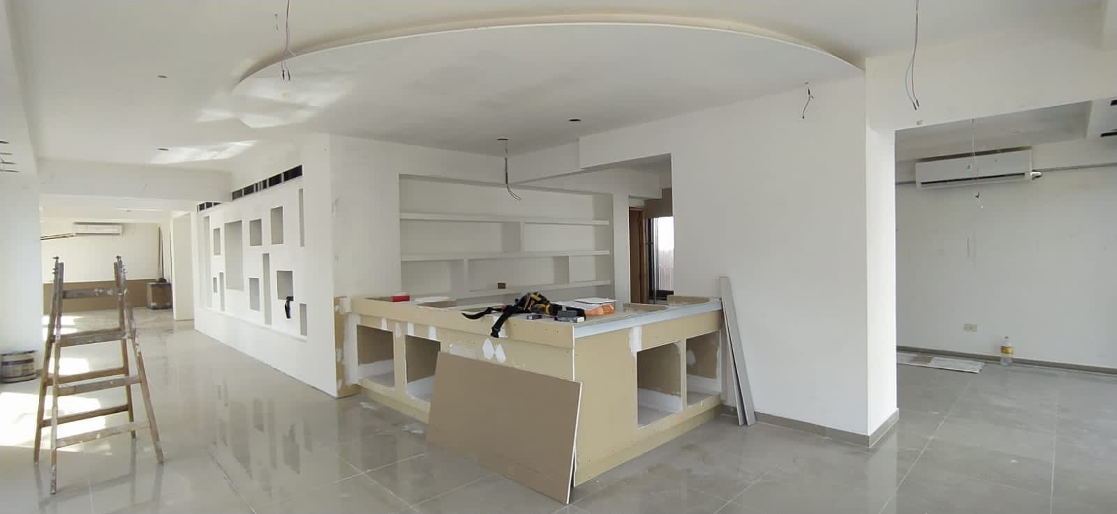 Habitación luminosa sin terminar, con paredes blancas, una escalera y un mostrador central en construcción