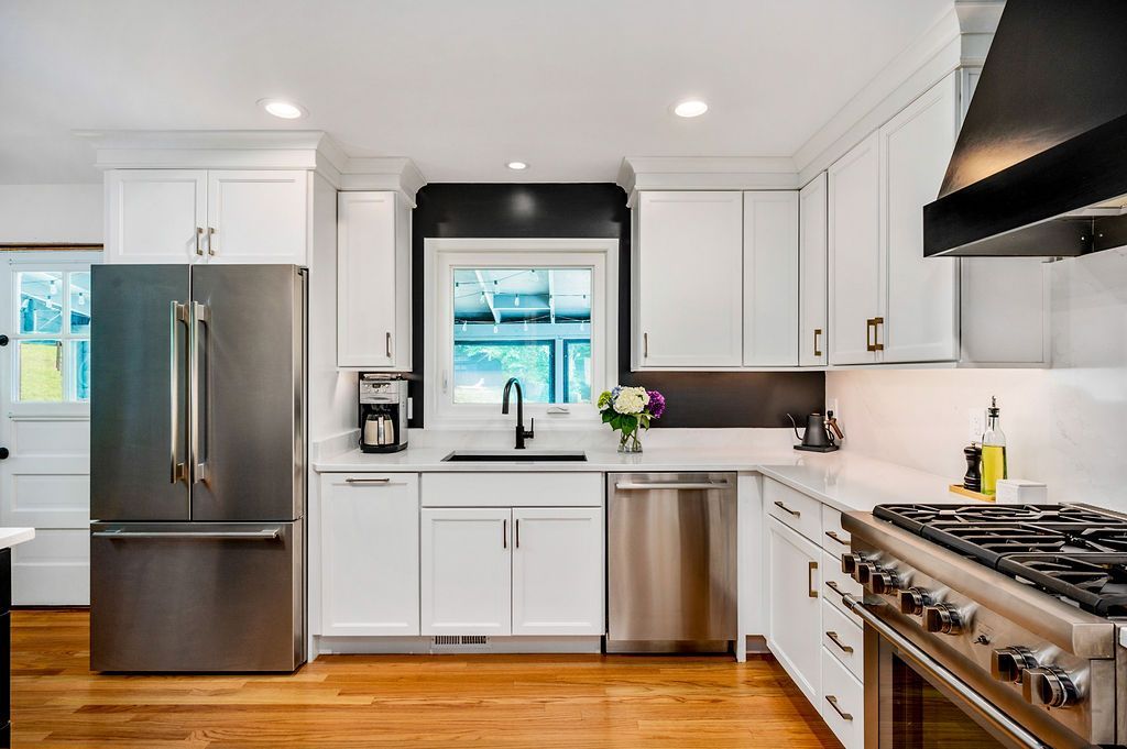 Modern kitchen with stainless steel appliances, white cabinets, and wooden floors.