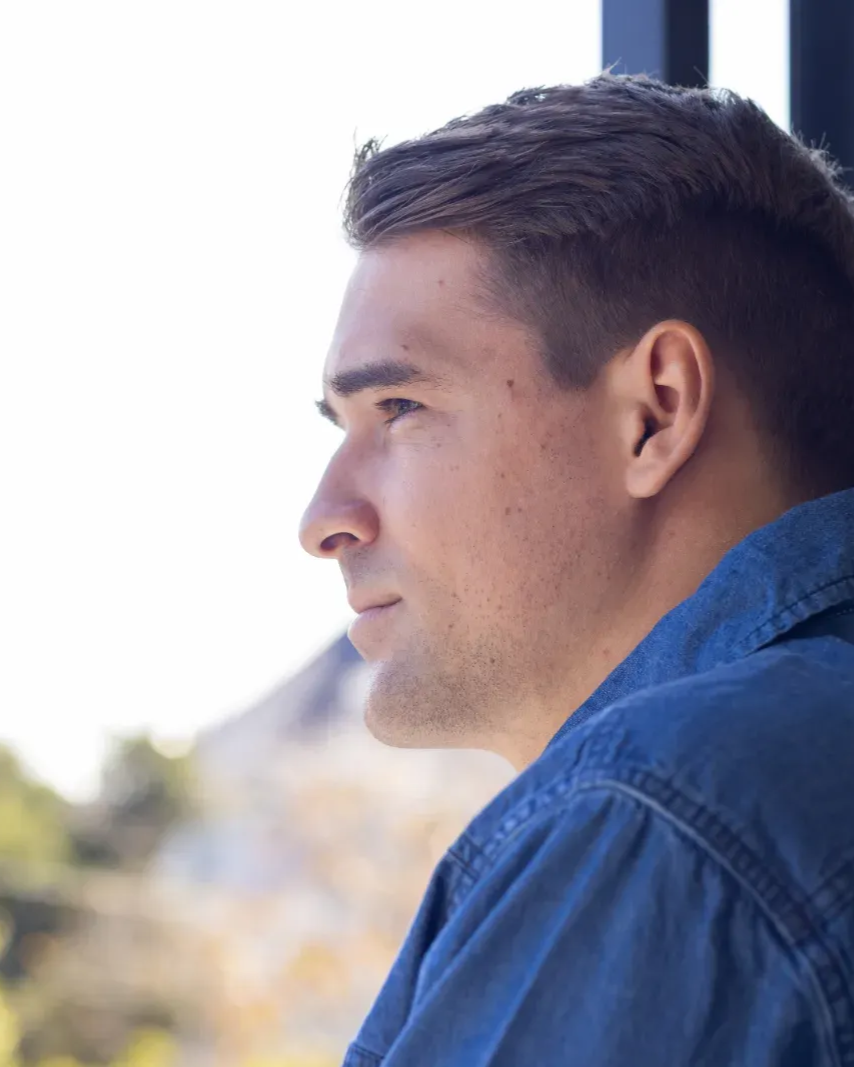 Profile of a man in a blue shirt looking left outdoors, with a blurred background