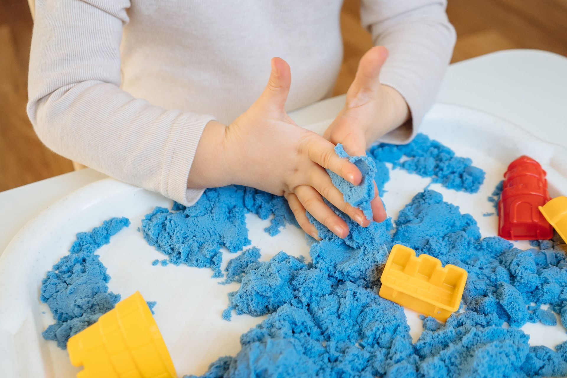 A child placing a small figure in a tray of sand during a sand tray therapy session
