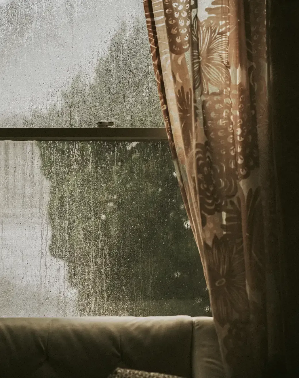 A rain-streaked window with a patterned curtain beside it