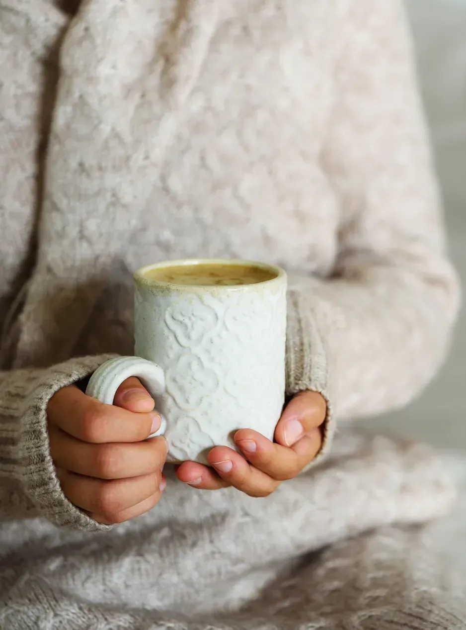 Hands holding a warm mug, wrapped in a soft knit sweater