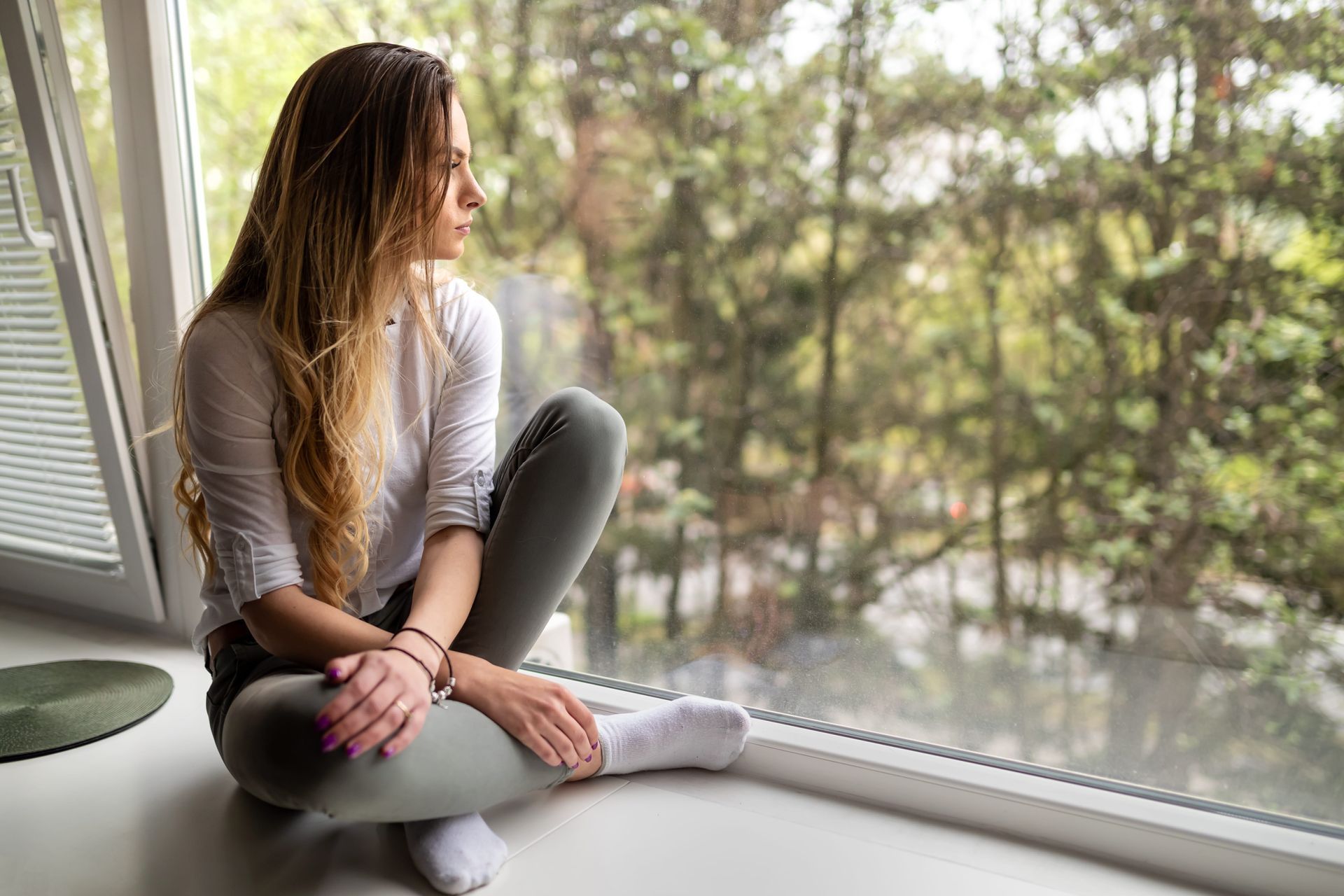 A woman sitting calmly by a window in Grimsby, reflecting, representing healing from nervous system