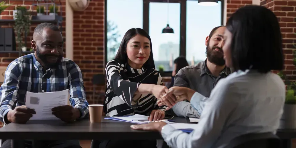 A group of people are sitting at a table shaking hands.