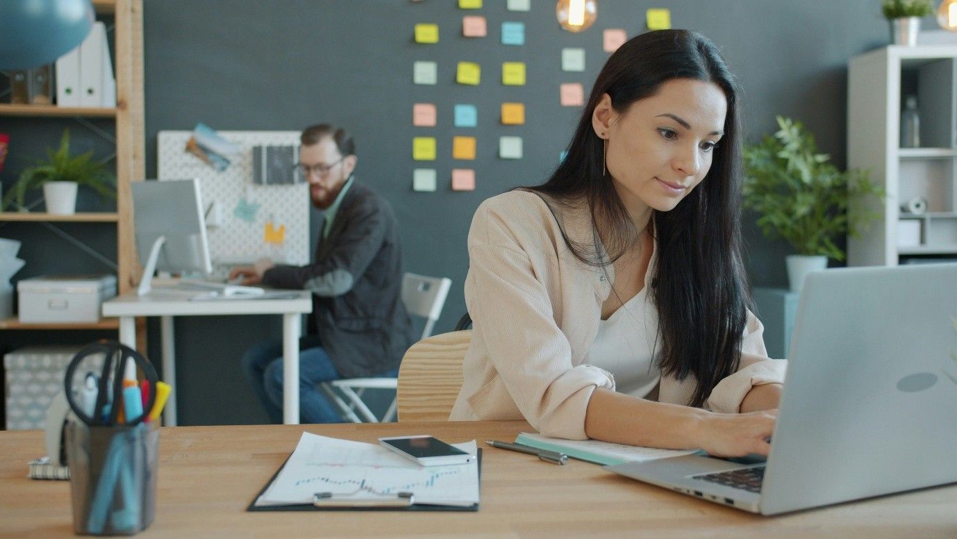 Woman working on her laptop and man working on his laptop on the background, office setting