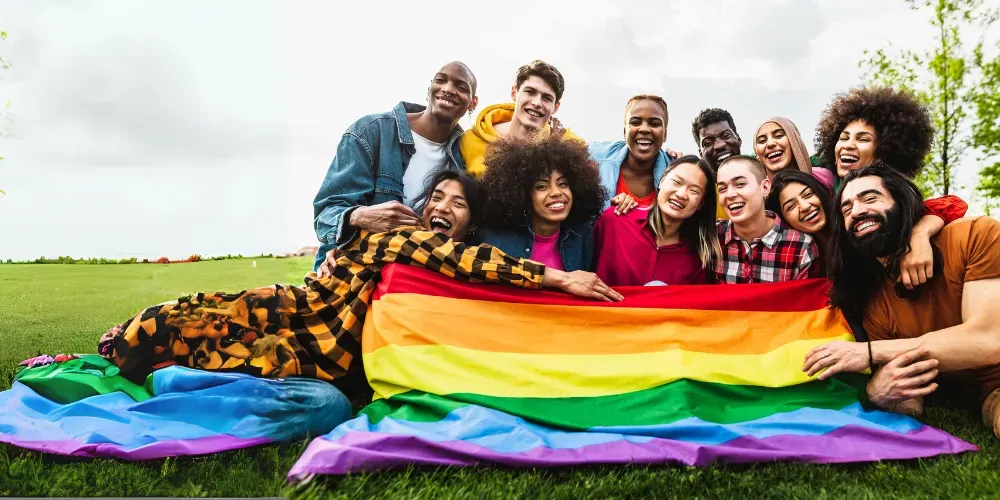 A group of people are sitting on the grass holding a rainbow flag.