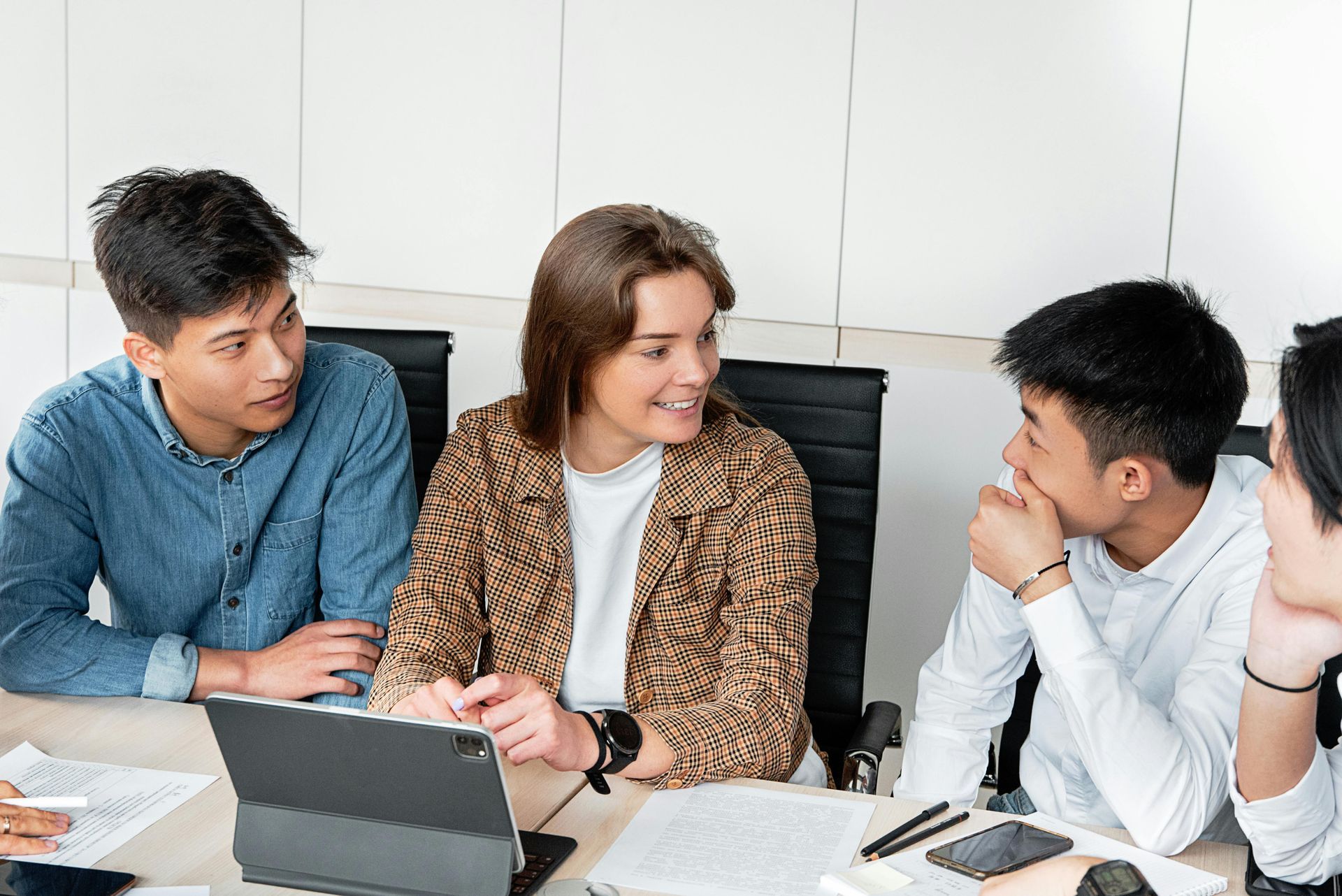 Group of young people in a meeting, talking and looking at a laptop on a table.