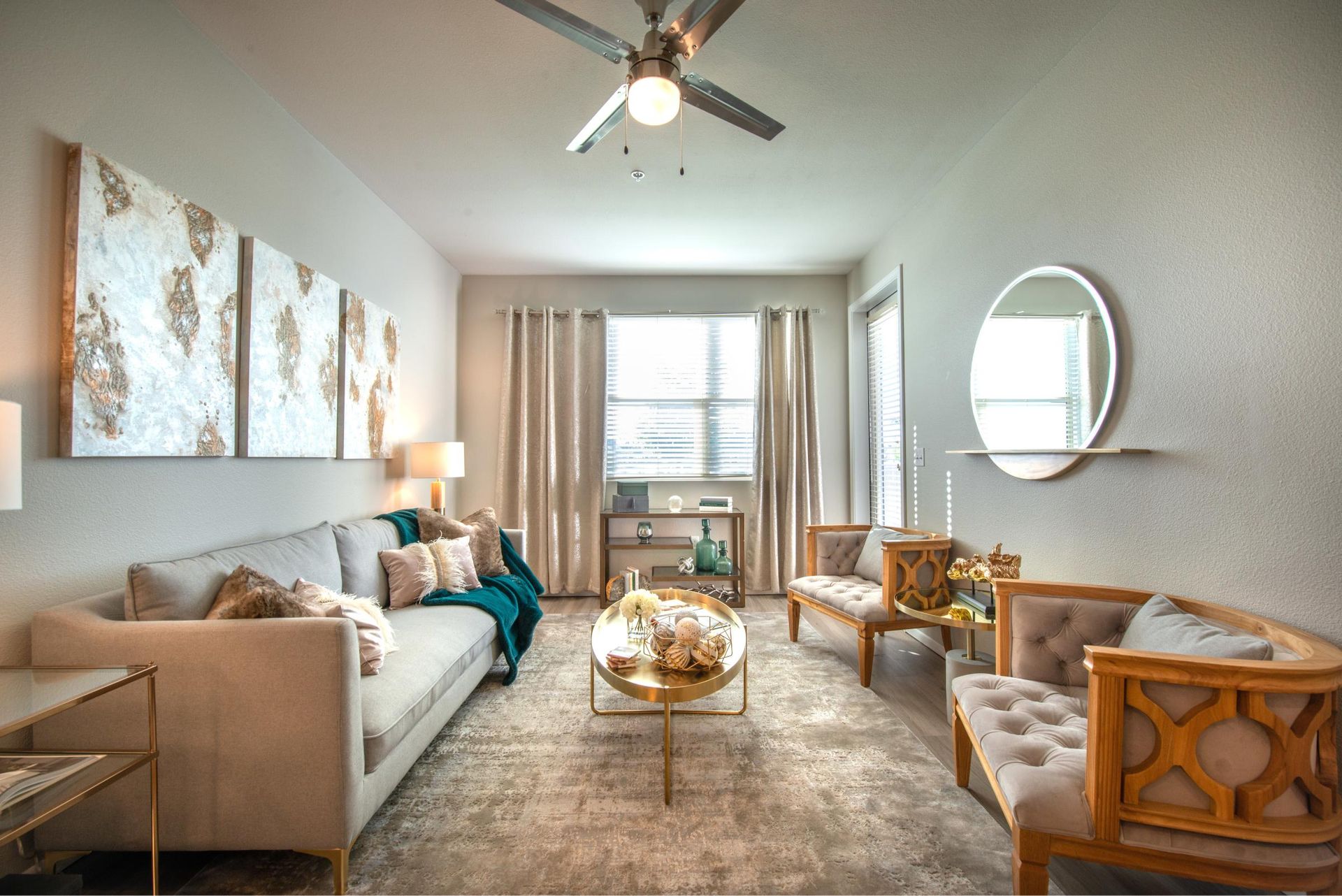 Bright living room in an apartment with beige sofa, upholstered chairs, coffee table, and large window.