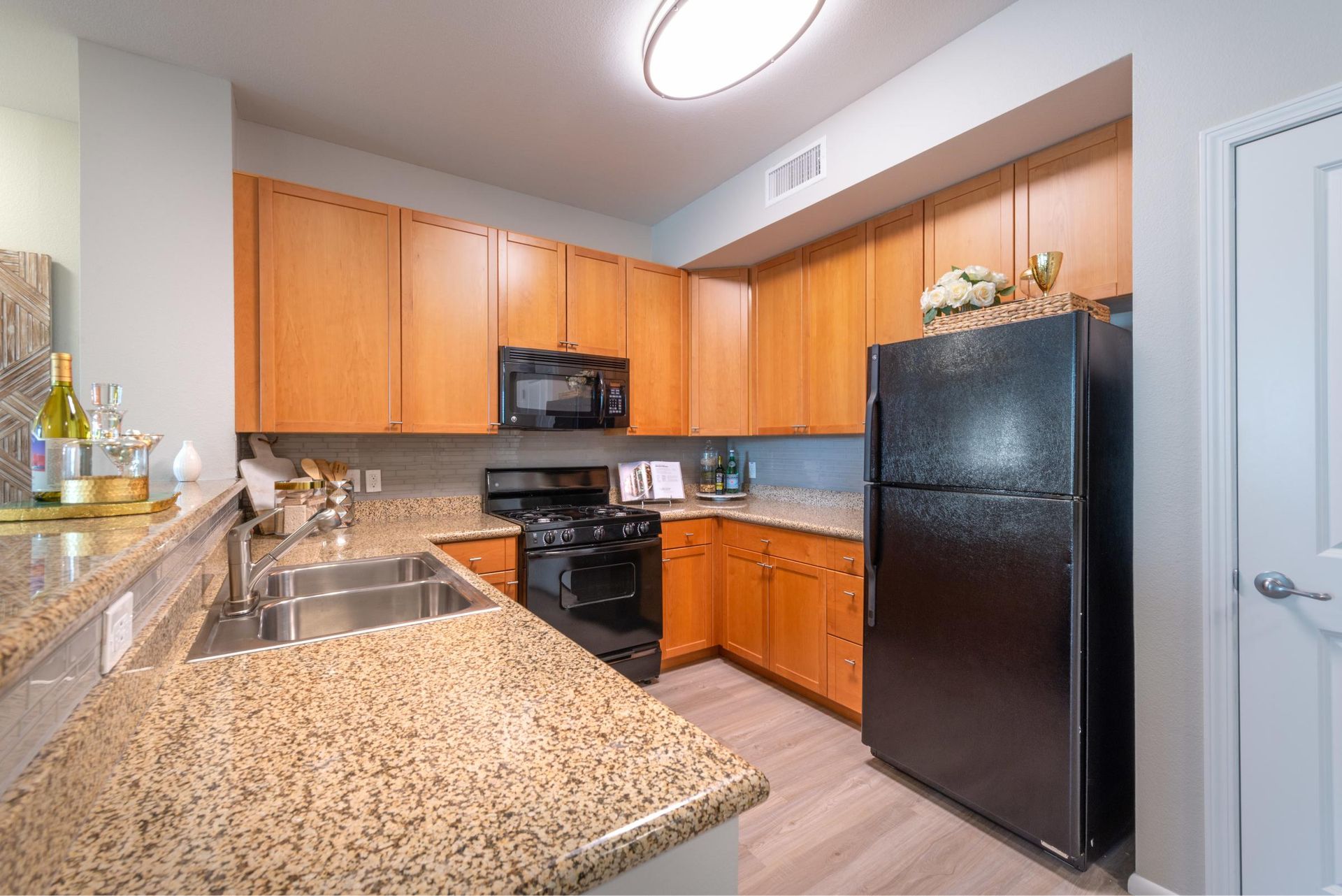 Modern apartment kitchen with granite countertops, wooden cabinets, a double sink, and black appliances.