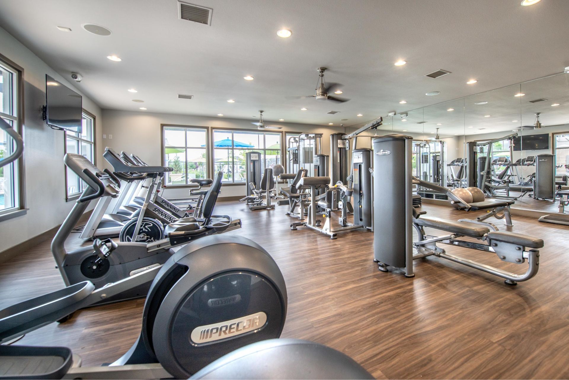 Bright apartment gym with treadmills, ellipticals, weights, and large windows.