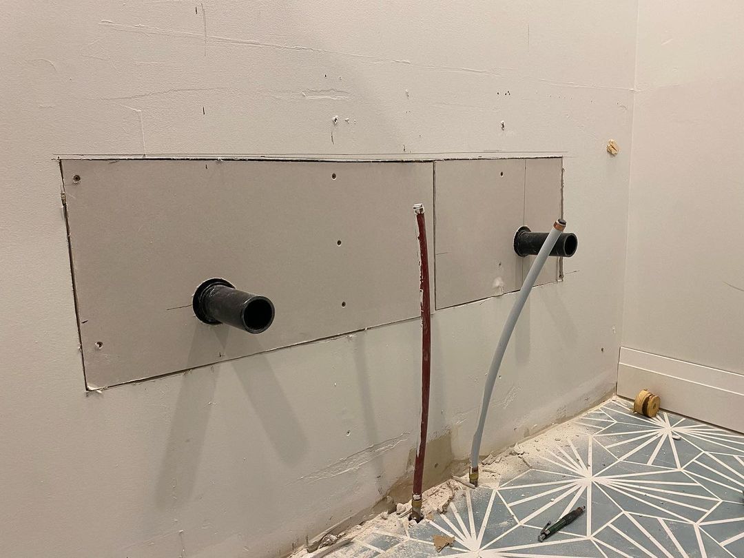 A bathroom is being remodeled and there are two pipes coming out of the wall.