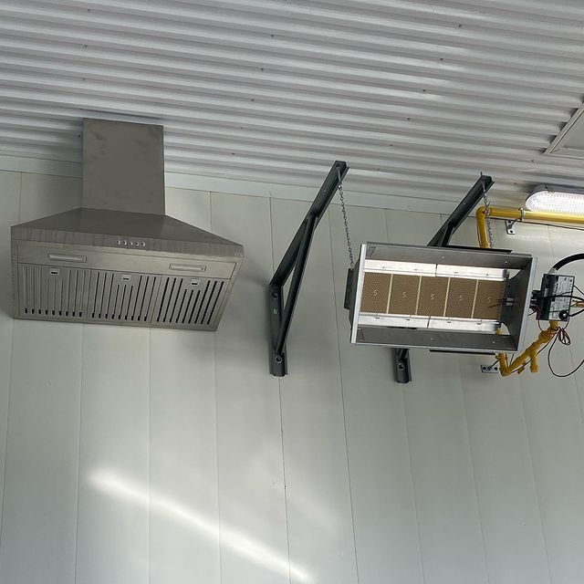 A stainless steel exhaust hood and a gas heater are mounted to a wall.