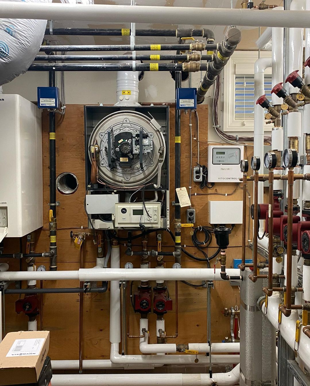 A room with a lot of pipes and a boiler on the wall.