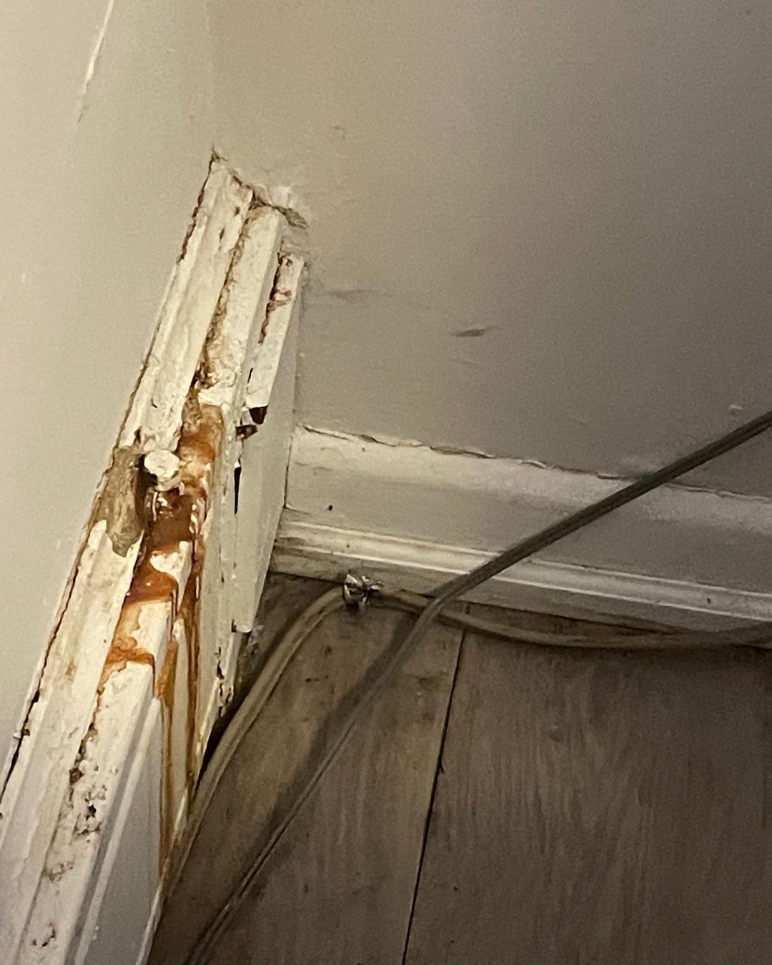 A corner of a wall with a hole in it and a wire coming out of it.