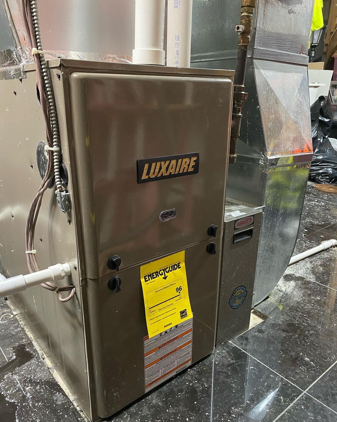 A stainless steel furnace is sitting on a tiled floor in a room.