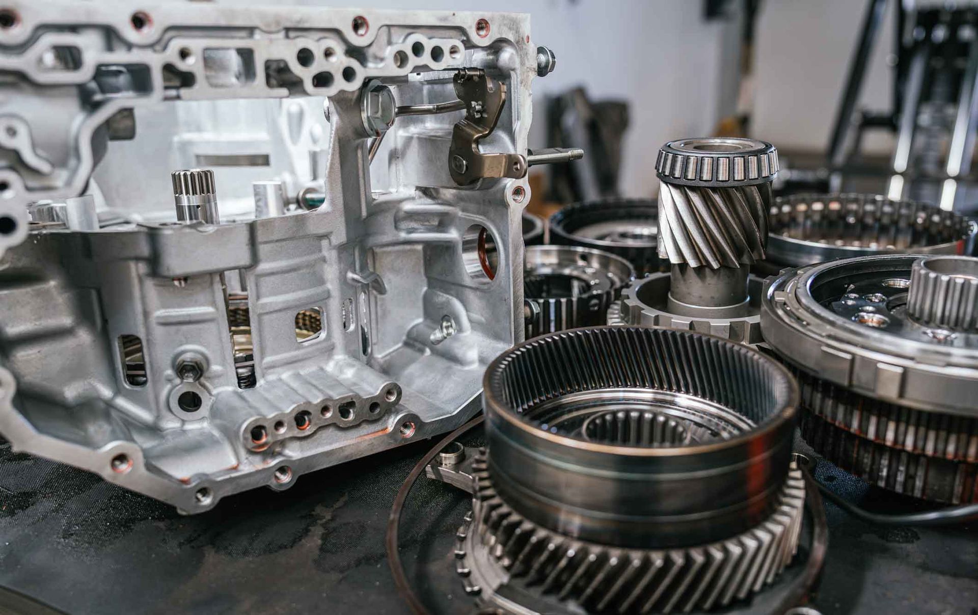 Automotive transmission housing beside disassembled gears and clutch components on a workbench