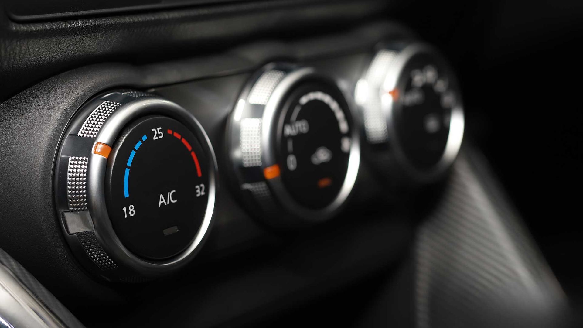 Car dashboard climate controls with three silver dials and blue-red temperature markings