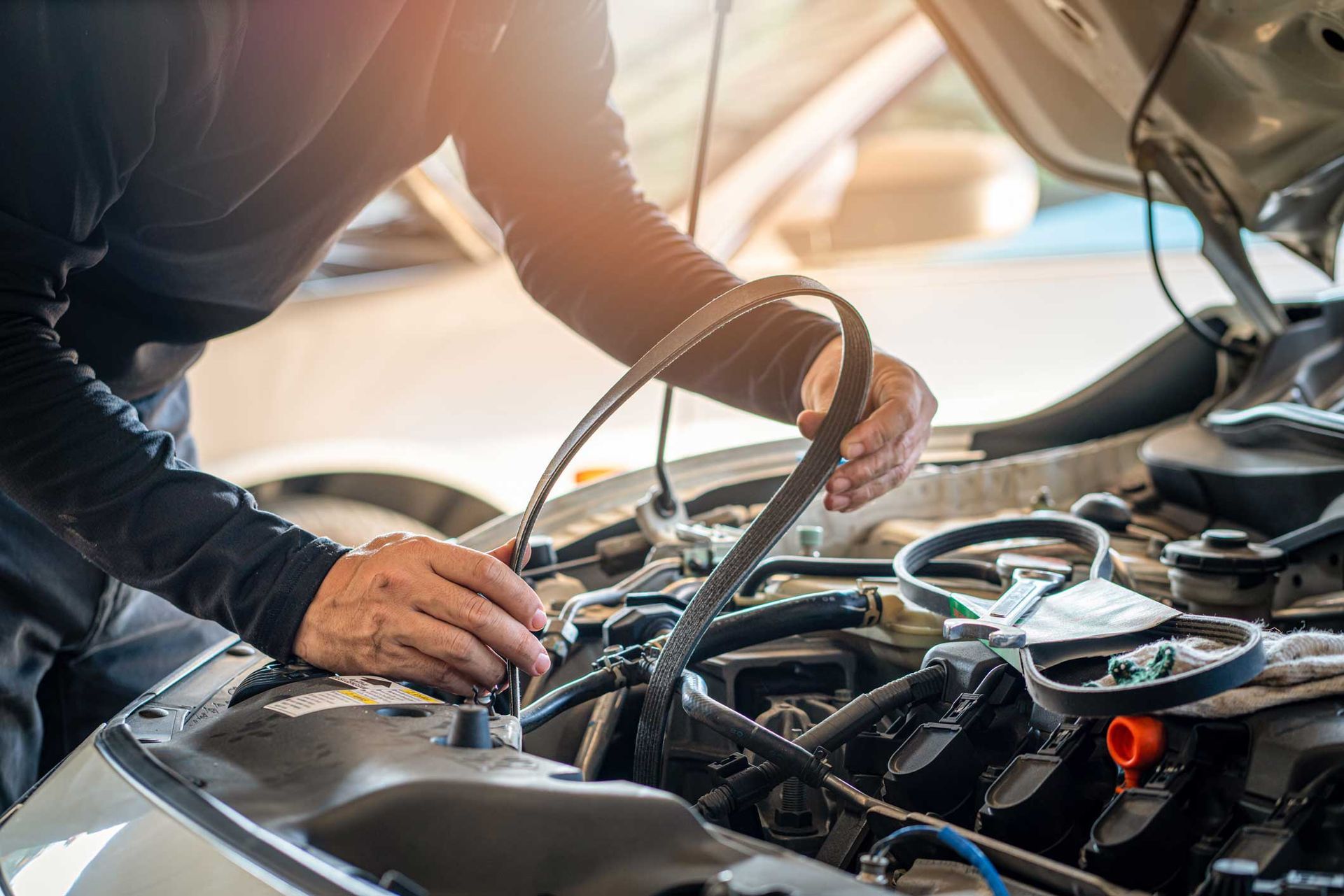 Mechanic working under a car hood, inspecting engine components with tools in a garage