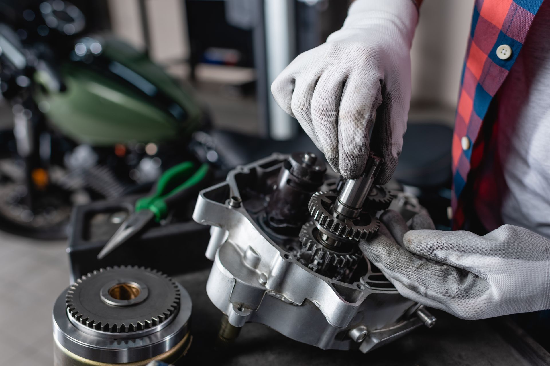 Gloved mechanic inspecting a car engine part on a workbench with tools nearby