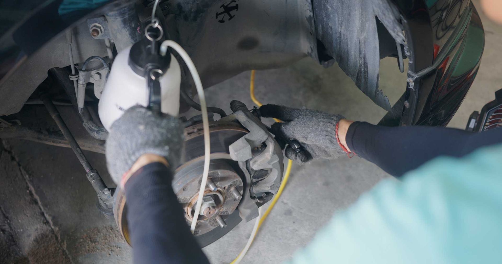 Two gloved workers handling cables and tools inside a vehicle wheel well