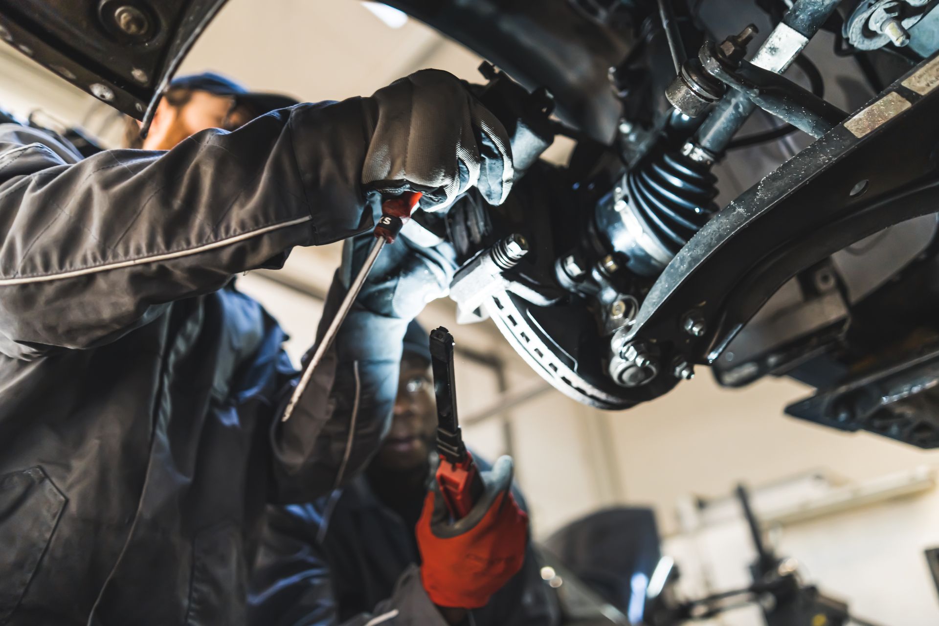Mechanic working under a car, using a tool near the suspension in a garage