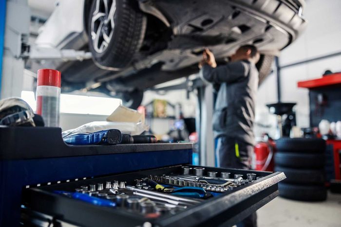 Auto mechanic working under a raised car in a busy repair shop with tools in the foreground Auto mechanic working under a raised car in a busy repair shop with tools in the foreground