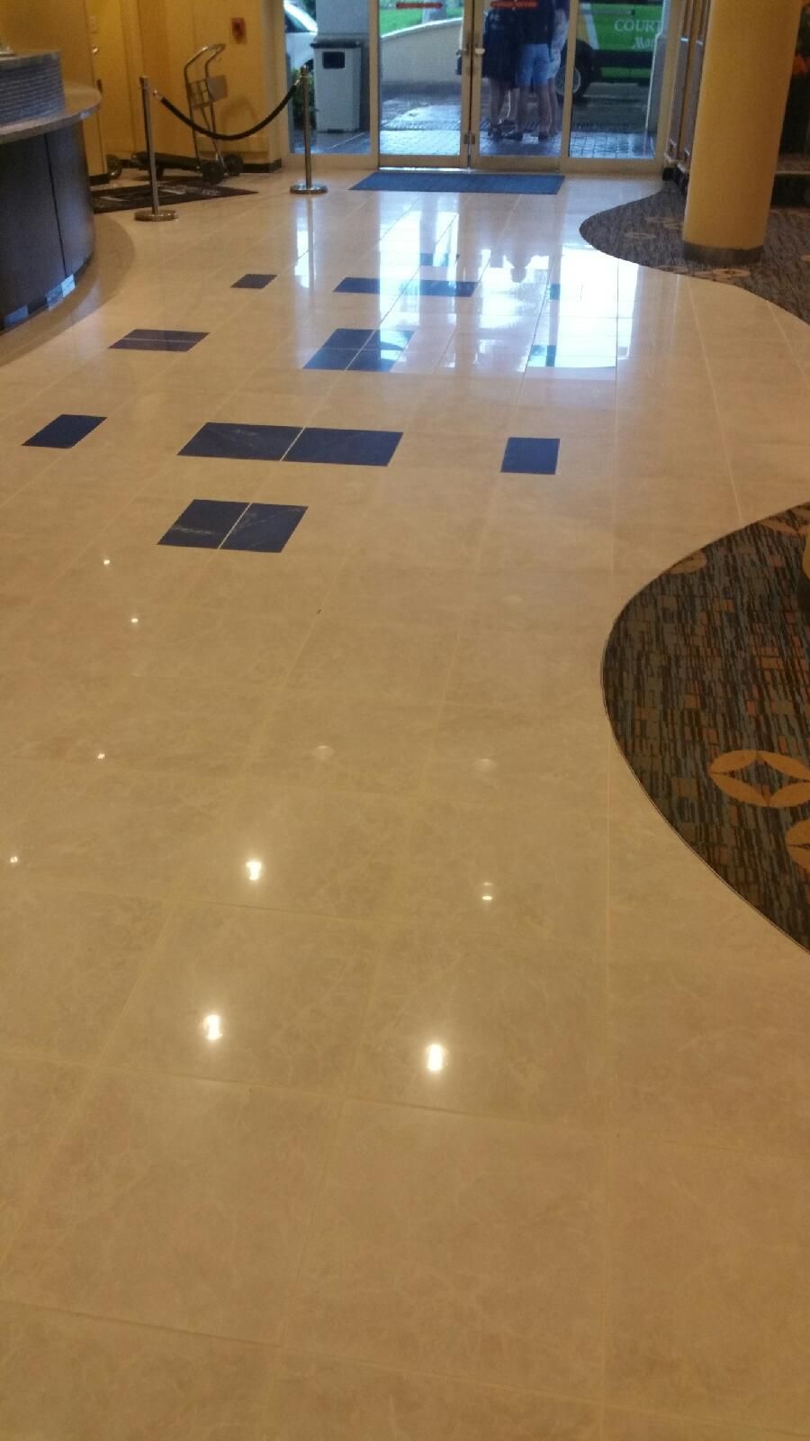 Shiny, light-colored marble floor with a few blue squares. A doorway with people is visible.
