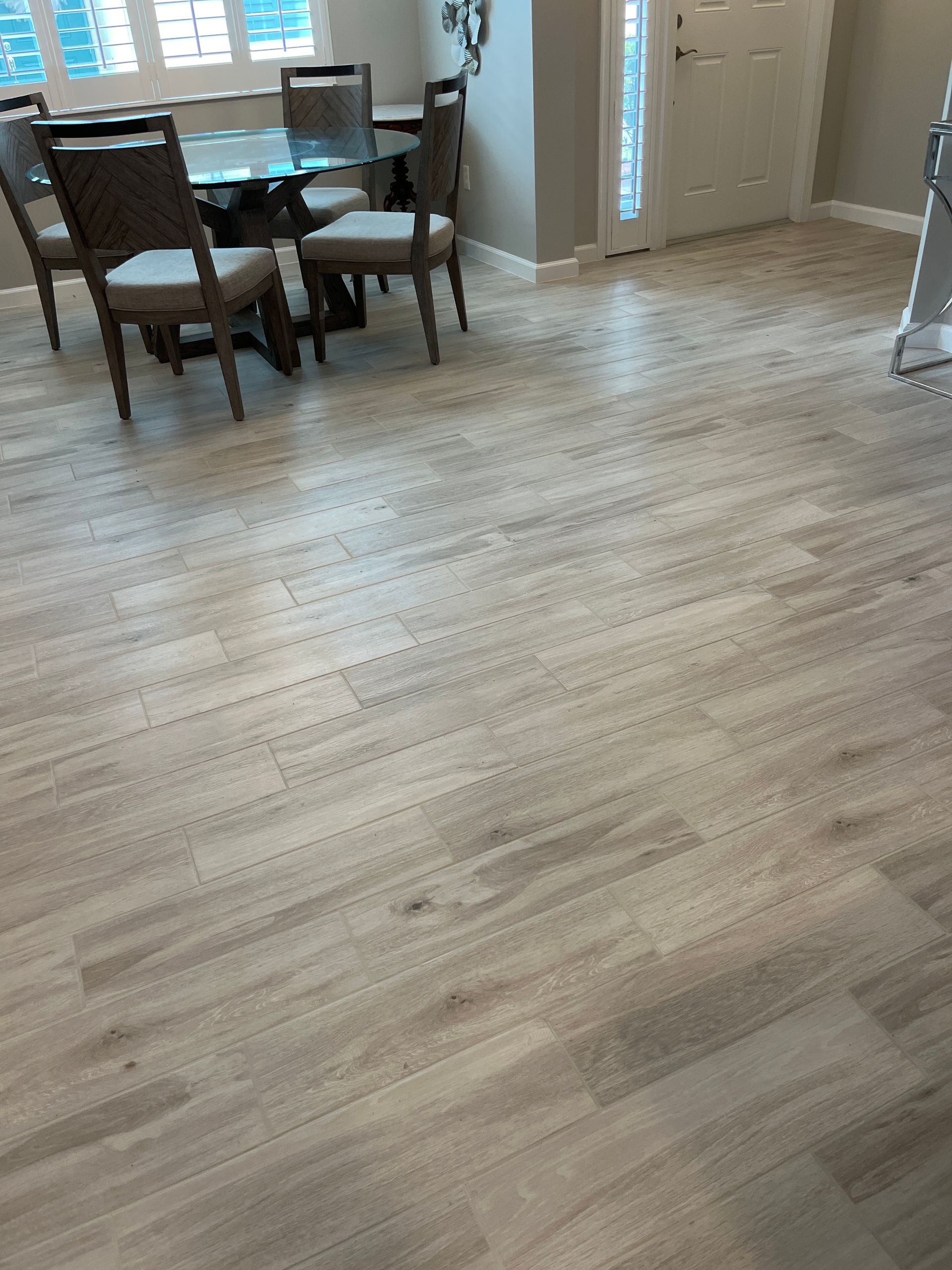 Wood-look tile flooring in a home, near a dining table and front door, in light beige tones.