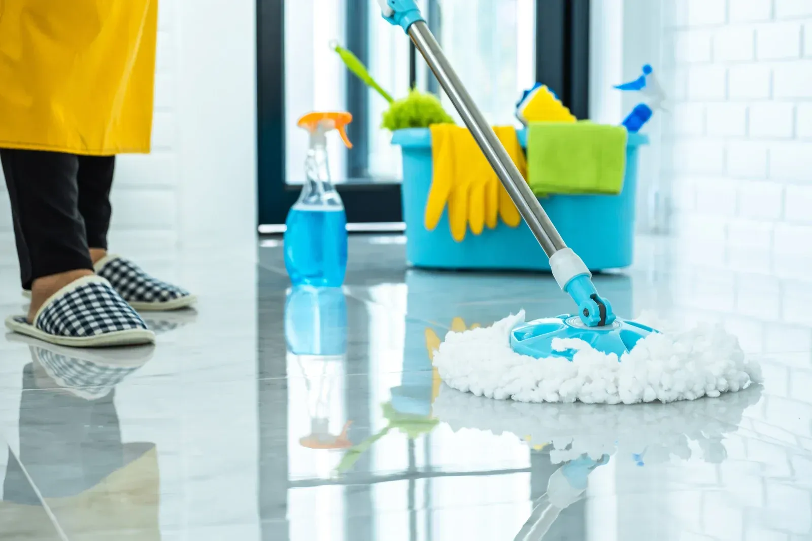 Person mopping a glossy, tiled floor with cleaning supplies nearby.
