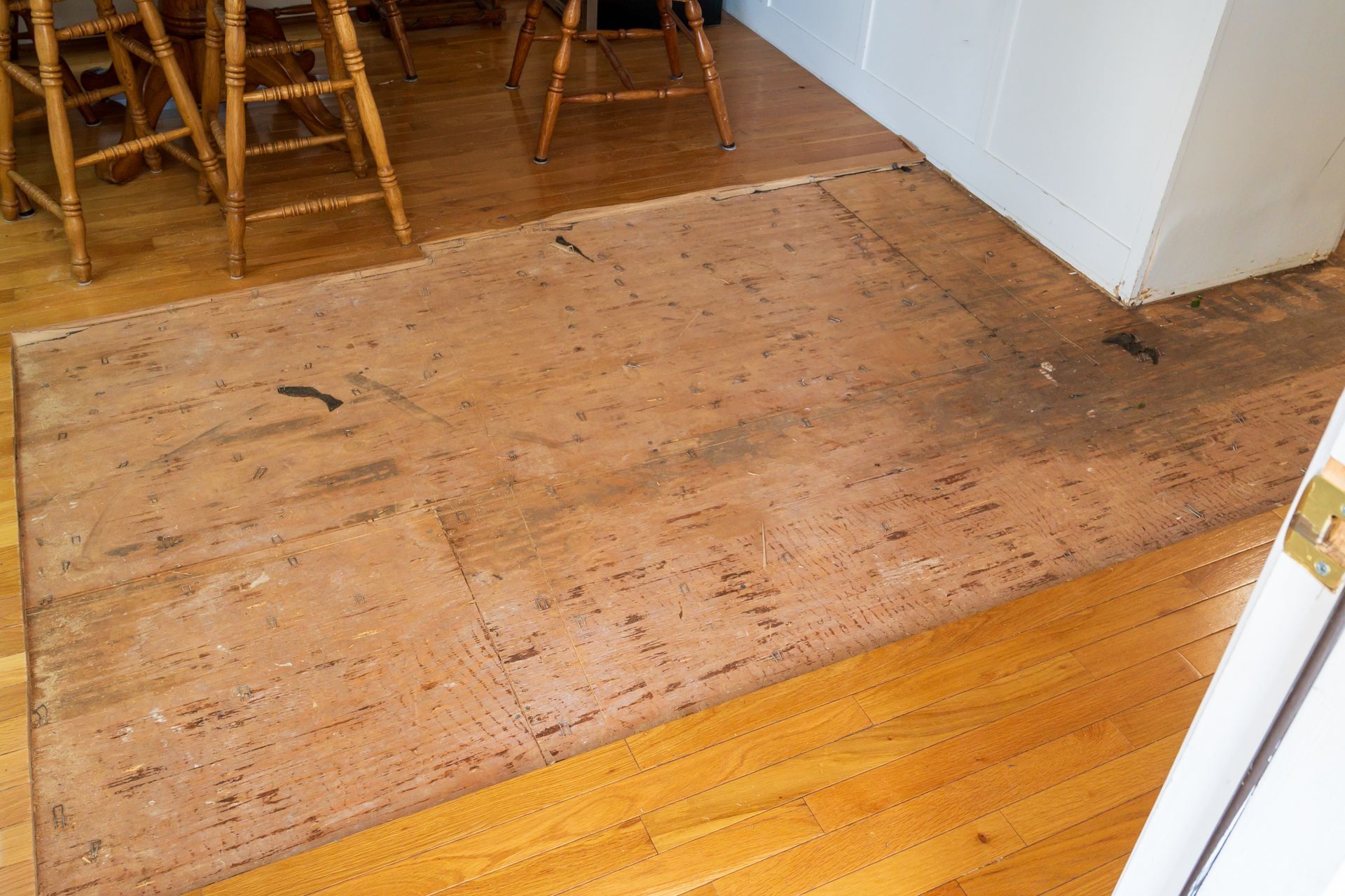Wooden floorboards with a dark, worn patch in a kitchen.