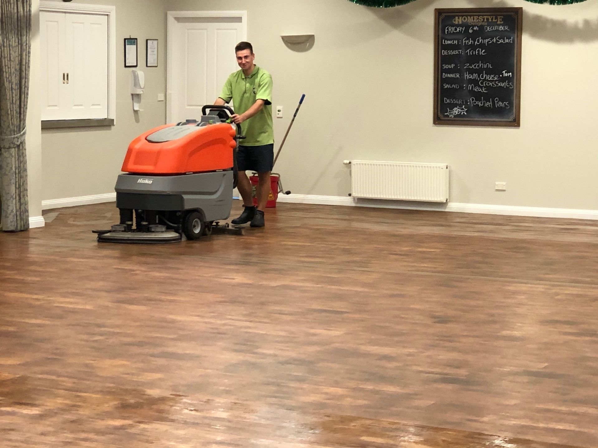 A man is cleaning a wooden floor with a machine.