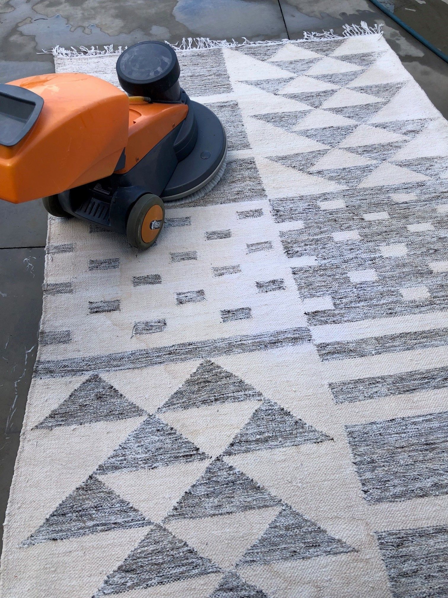 A machine is cleaning a rug on a concrete floor.