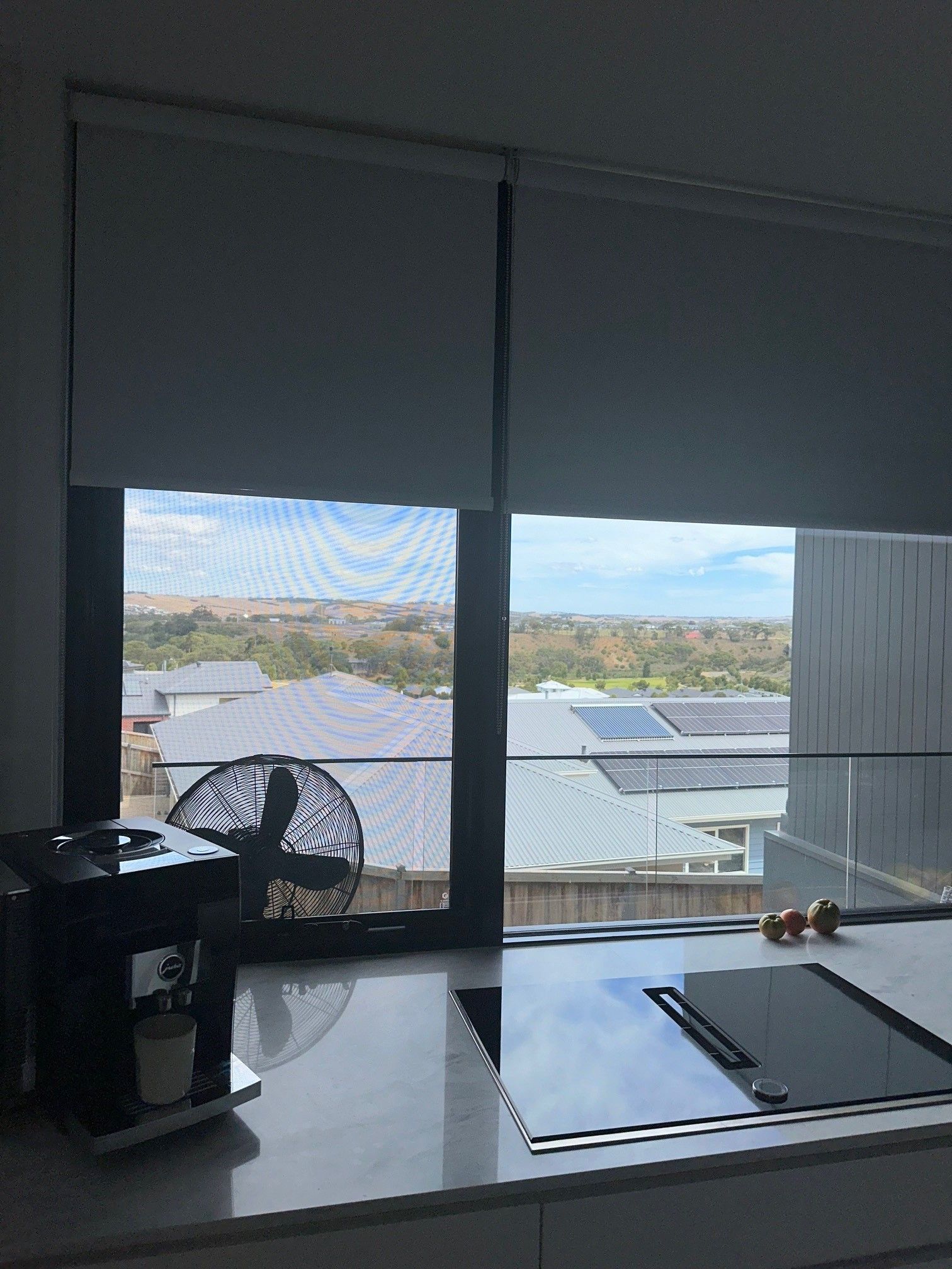 A kitchen counter with a fan and a window with blinds.