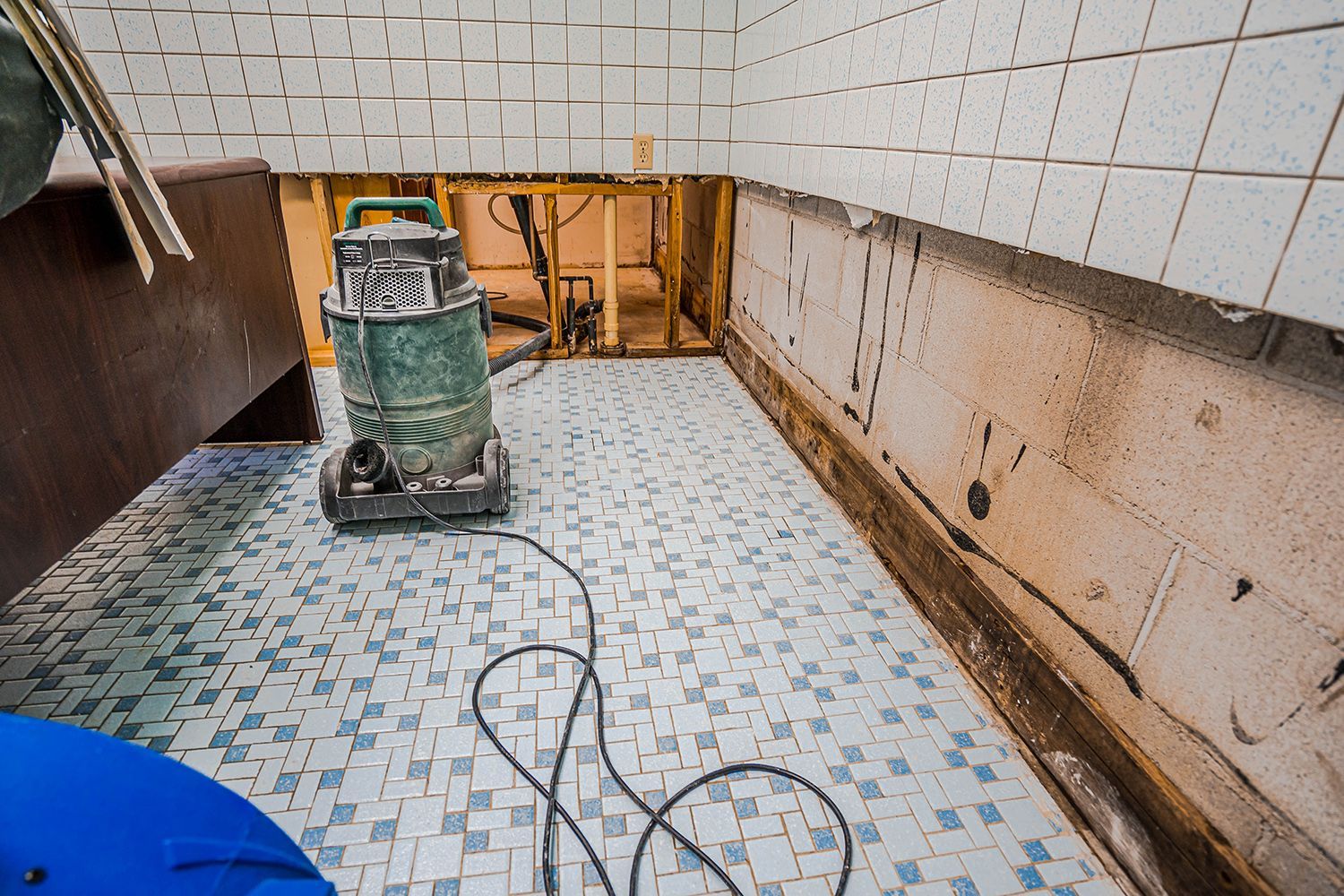 A bathroom featuring a green vacuum cleaner positioned on the floor to clean up flooding. A bathroom featuring a green vacuum cleaner positioned on the floor to clean up flooding.