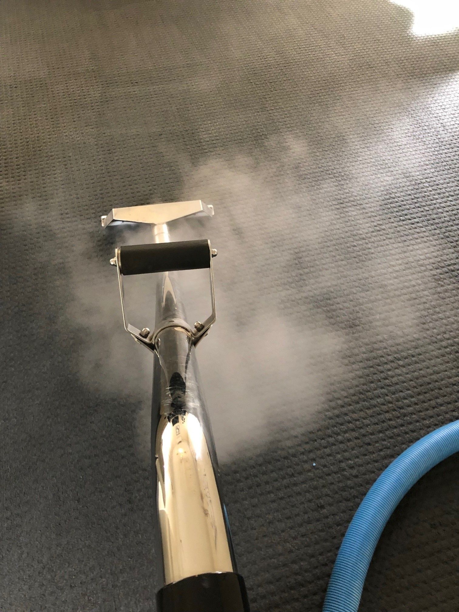 A carpet cleaner is cleaning a carpet with steam coming out of it.