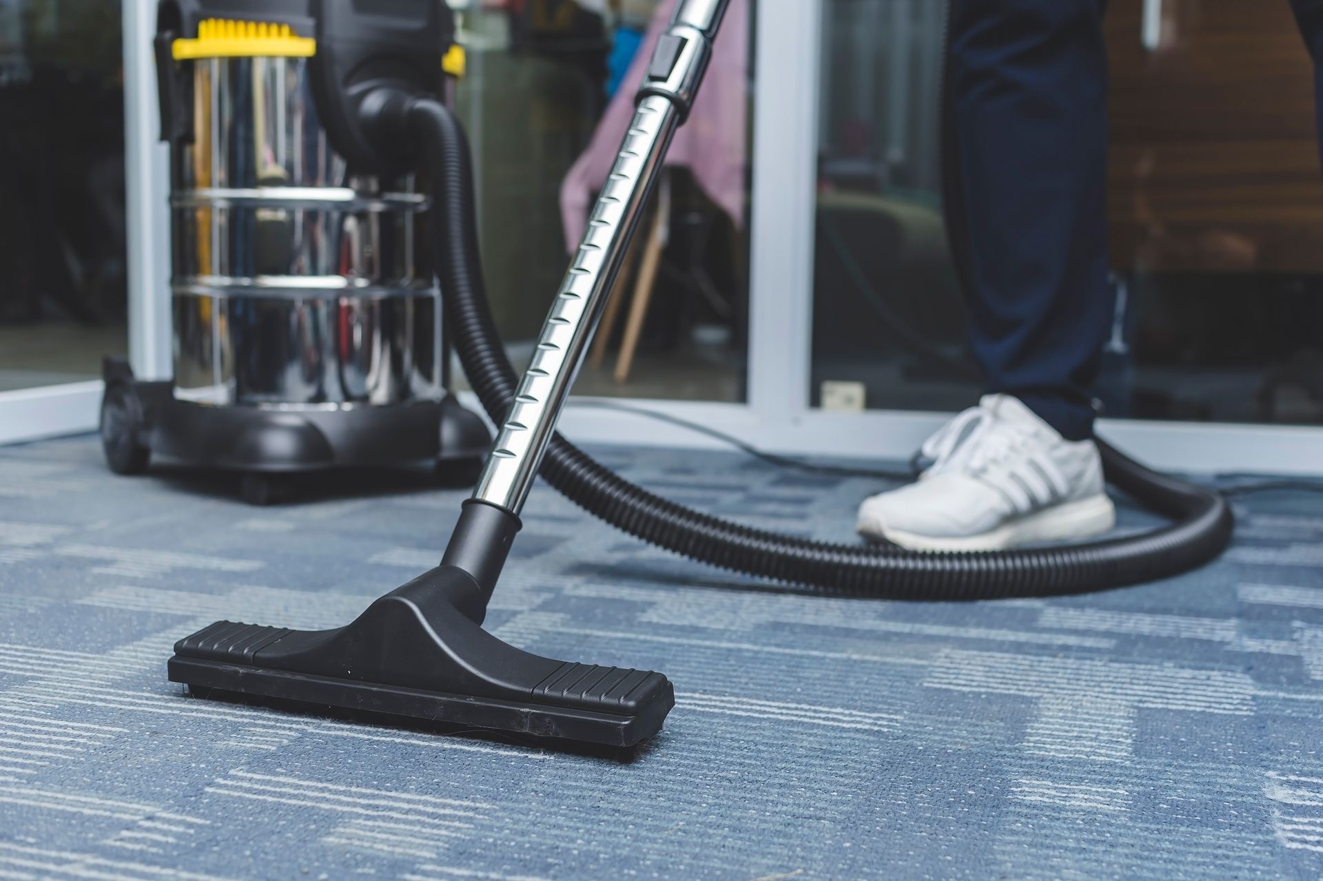 Technician performing commercial carpet cleaning with upright vacuum in office.