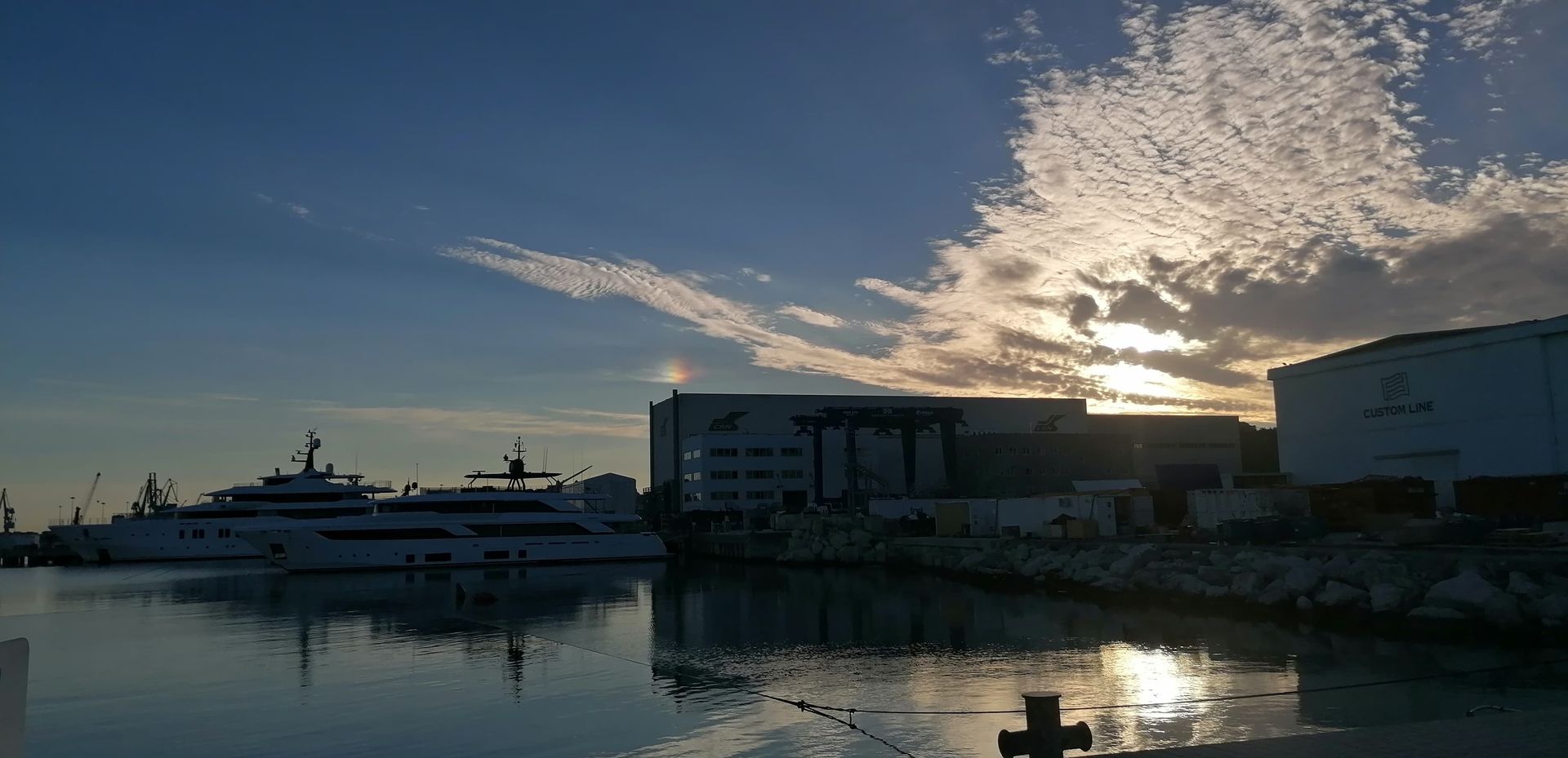 Yacht in un porto al tramonto, con edifici e cielo nuvoloso.